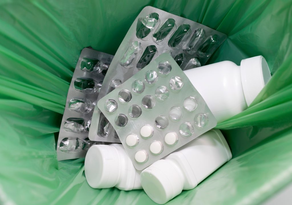 Empty blister packs and white pill bottles in a green trash bag.